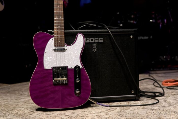 Violette E-Gitarre mit Boss-Verstärker und Kabeln auf einer Bühne